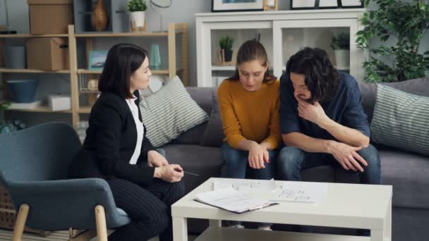 Immobilienmakler zeigt Hauspläne einem schönen Paar, das sich zu Hause unterhält — Stockvideo
