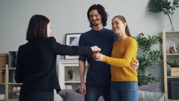 Chica y chico tomando llaves de la vivienda agente estrechando las manos besándose y abrazándose — Vídeos de Stock