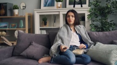 Genç Bayan izlerken TV gülüyor ve yeme Popcorn evde yalnız eğlenmek