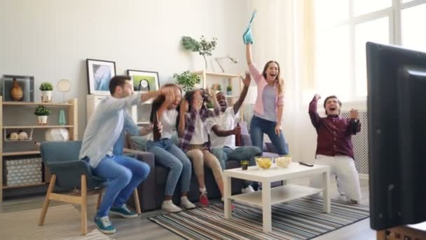 Multiracial grupo viendo deportes en la televisión en casa animando haciendo high-five abrazos — Vídeo de stock