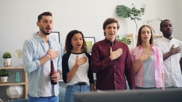 Students patriots singing national anthem watching sports game on TV at home — Stock Video