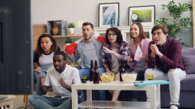 Genç Kanadalılar TV 'de hokey maçı izliyor bayraklarla tezahürat yapıyorlar ve beşlik çakıyorlar.