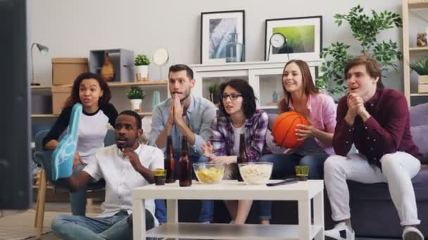 Мультиэтническая группа молодых людей смотрит баскетбол по телевизору дома — стоковое видео