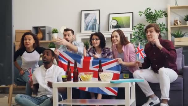 Chicas y chicos británicos viendo deportes en la televisión ondeando banderas celebrando la victoria — Vídeo de stock