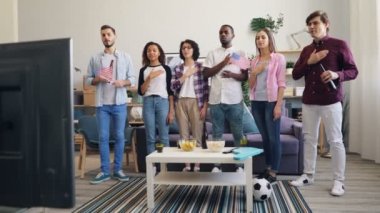 Amerikan marşı nı söyleyen kadın ve erkekler televizyonda evde futbol seyrederken bayrak sallıyor