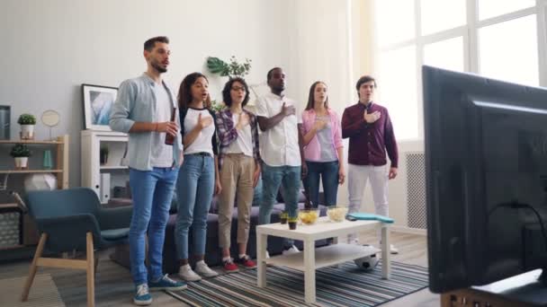 Football fans singing national anthem standing indoors watching match on TV — Stock Video