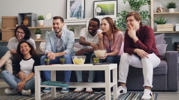 Chicas y chicos disfrutando de la comedia en la televisión riendo y comiendo palomitas de maíz en casa — Vídeo de stock