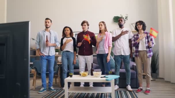 Giovani spagnoli che cantano inno sventolando bandiera guardando la partita in TV in appartamento — Video Stock