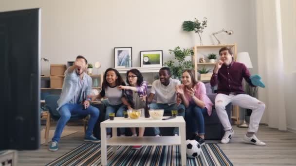 Amigos felizes assistindo esportes em casa dançando e rindo celebrando a vitória — Vídeo de Stock