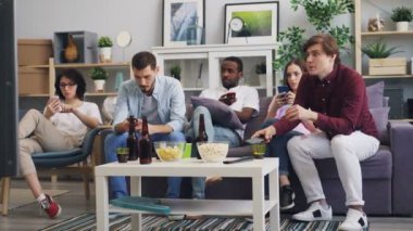 Akıllı telefon kullanan kadın ve erkekler daha sonra evde birlikte Tv'de haber izliyor