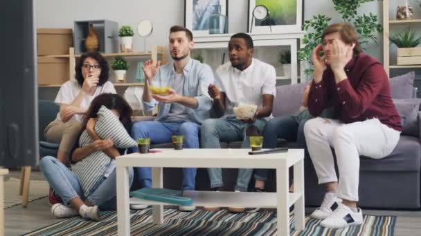 Scared young people students watching thriller on TV and eating snacks at home — Stock Video