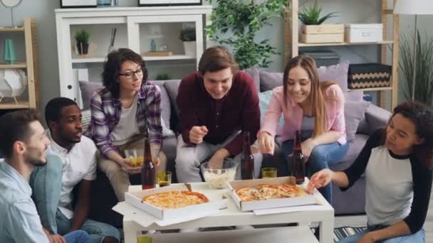 Οι φίλοι παίρνουν φέτες από πίτσα που μυρίζει φαγητό στο εσωτερικό πάρτι στο σπίτι — Αρχείο Βίντεο