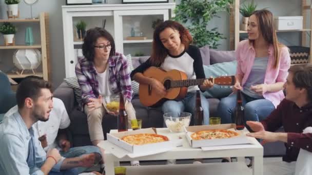 Chicas y chicos cantando tocando la guitarra divirtiéndose en la fiesta en piso moderno — Vídeo de stock