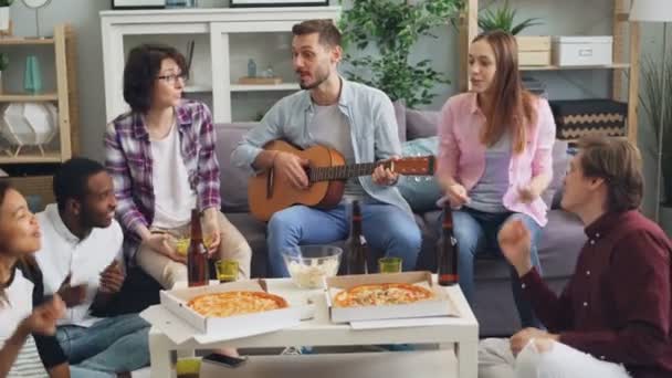 Erkek ve kadın arkadaşlar gitar çalıyor ve evde partide birlikte şarkı söylüyor — Stok video