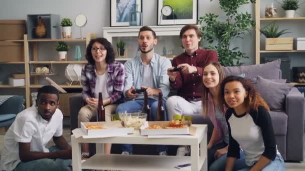 Χαρούμενοι τύποι παίζουν παιχνίδι βίντεο, ενώ οι φίλοι βλέποντας και γελώντας στο σπίτι — Αρχείο Βίντεο
