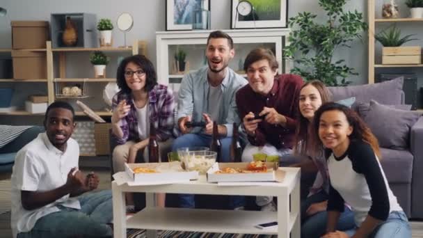 Νέοι άνδρες που διασκεδάζουν με βιντεοπαιχνίδι στο σπίτι ενώ οι φίλοι παρακολουθούν — Αρχείο Βίντεο