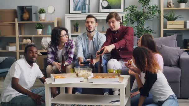Mladí šťastní přátelé hrát videohry mluvit jíst baví doma párty — Stock video