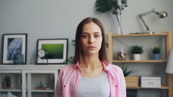 Медленный портрет серьезной молодой женщины, смотрящей в камеру, стоящую дома — стоковое видео
