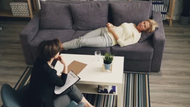 Високий кут зору жінки, що поділяє проблеми з терапевтом, лежачи на дивані в офісі — стокове відео