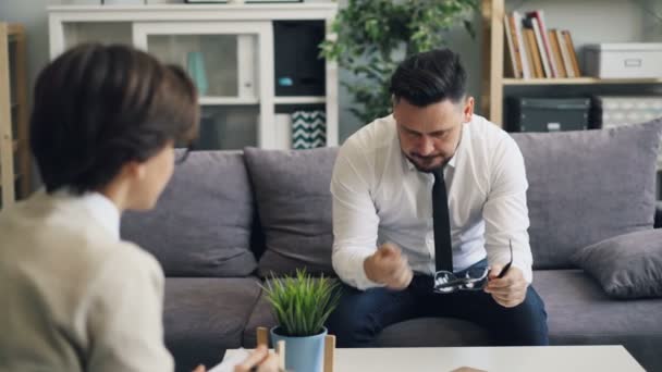 Депрессивный мужчина плачет во время разговора с психологом в современном офисе — стоковое видео