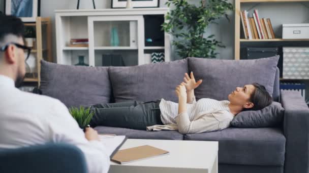 Młoda kobieta rozmawia z psychologiem leżącym na kanapie w biurze, rozmawiając gestykulując — Wideo stockowe