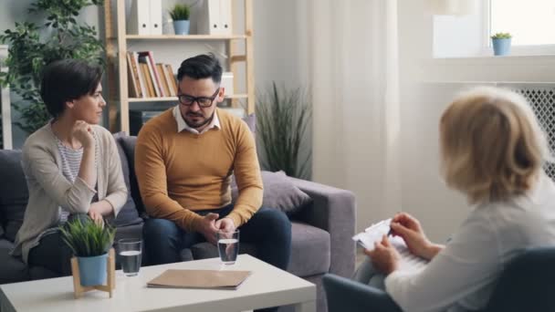 Zły młoda kobieta rozmawia z mężem w biurze psychoterapeutów podczas sesji — Wideo stockowe