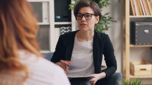 Успешный терапевт обсуждает проблемы с клиентом, сидящим в офисе вместе — стоковое видео