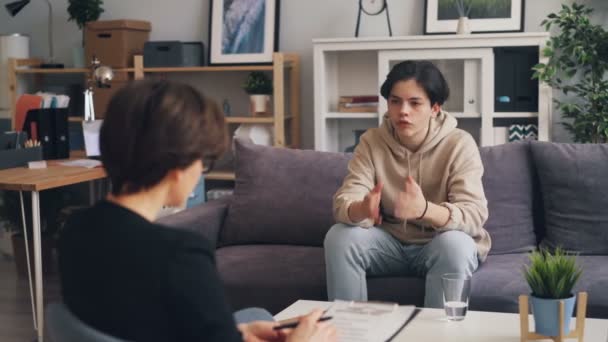Chico estresado adolescente hablando con una joven psicóloga en el consultorio — Vídeo de stock