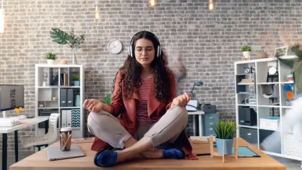 Час переплетення дівчини, що слухає музику в позі лотоса на столі в навушниках — стокове відео