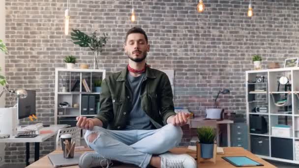 Zoom in time-lapse of guy meditating sitting on office desk in lotus position — 비디오