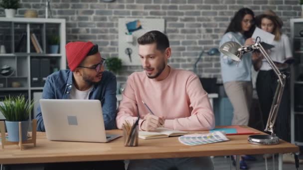 Junge Männer diskutieren Projekt mit Blick auf Laptop-Bildschirm im kreativen modernen Büro — Stockvideo