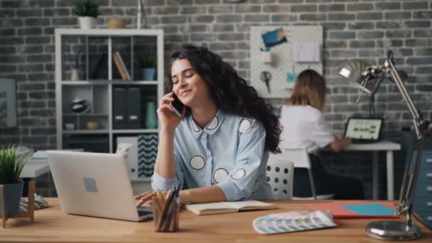 Mosolygó asszony beszél a mobiltelefonról irodai dolgozó laptop at Desk — Stock videók