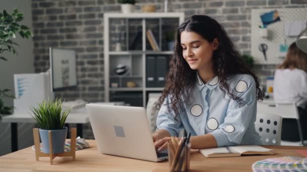 Muchacha atractiva usando el ordenador portátil mirando la escritura de pantalla y sonriendo en la habitación de la oficina — Vídeos de Stock