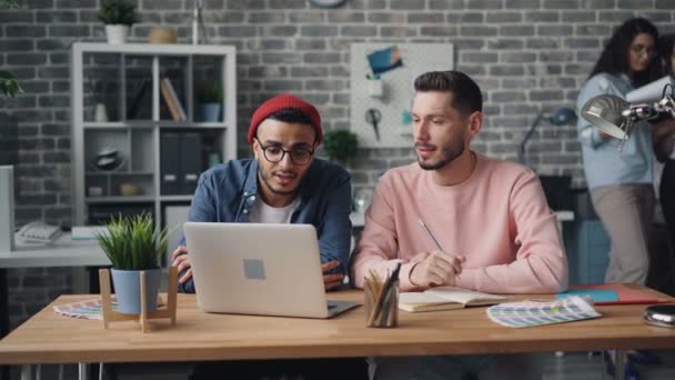 Jongens collega's spreken kijken naar laptop scherm werken in Office samen — Stockvideo