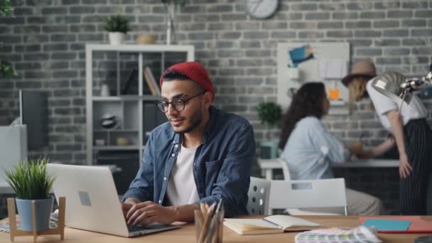 Χαρούμενο νεαρό άντρα χρησιμοποιώντας το laptop πληκτρολόγηση που εργάζονται σε μοντέρνο στυλ σοφίτα γραφείο — Αρχείο Βίντεο