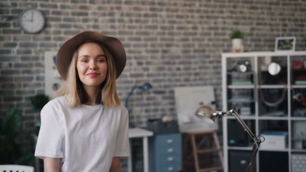 Retrato de linda chica en sombrero de pie en la oficina solo sonriendo mirando a la cámara — Vídeo de stock