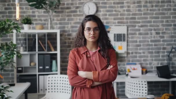 Портрет серьезной молодой женщины, стоящей в офисе в одиночестве со скрещенными руками — стоковое видео