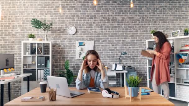 Time-lapse di ragazza stressata seduta alla scrivania toccare la testa quando i colleghi in movimento — Video Stock