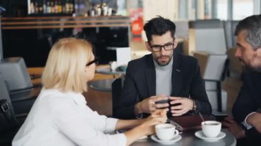 Sakallı işadamı modern kafede erkek ve kadın partnerleri ile konuşuyor