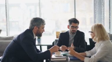 Sakallı adamlar kafede üst düzey iş kadını ile sözleşme detayları tartışıyor
