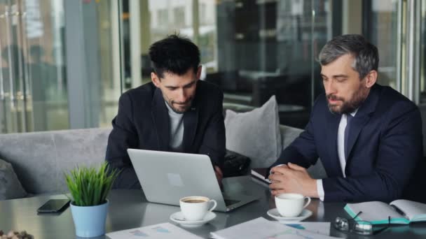 Οι επιχειρηματικοί εταίροι διαπραγματεύονται συμβόλαια μιλώντας κοιτάζοντας την οθόνη του φορητού υπολογιστή στο καφέ — Αρχείο Βίντεο