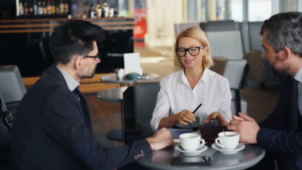 Улыбающаяся деловая женщина обсуждает работу с партнерами-мужчинами во время встречи в кафе — стоковое видео