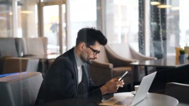 Kafede kahve molası sırasında akıllı telefon kullanan gözlüklü kendine güvenen sakallı adam