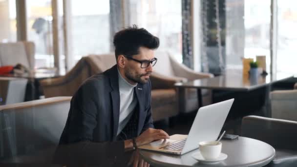 Male freelancer working in cafe using laptop looking at screen touching keyboard — Stock Video