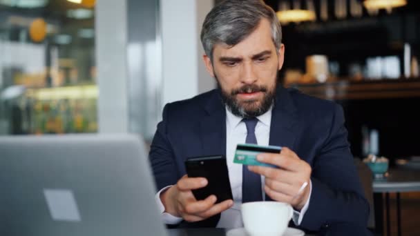 Empresario haciendo pago en línea con tarjeta de crédito y teléfono inteligente en la cafetería — Vídeo de stock