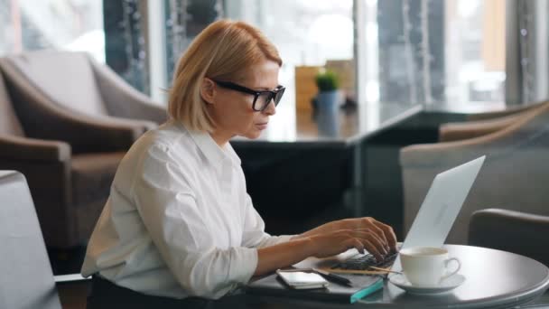 Femme d'affaires senior travaillant avec un ordinateur portable dans un café en tapant à l'écran — Video