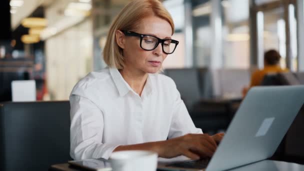 Kurumsal yönetici olgun bayan kafe de iş e-posta yazarak dizüstü bilgisayar ile çalışan — Stok video