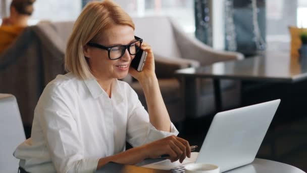 Hermosa dama de negocios hablando en el teléfono móvil portátil de comprobación y portátil — Vídeo de stock