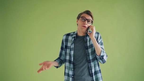 Joven alegre hablando por teléfono móvil y haciendo gestos sobre fondo verde — Vídeo de stock