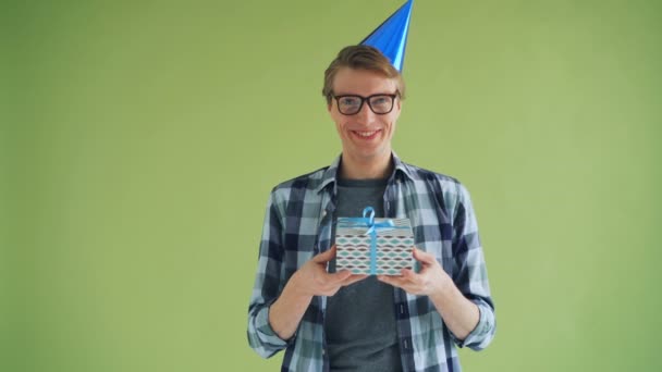 Retrato de cara feliz em chapéu de festa segurando presente de aniversário e rindo — Vídeo de Stock